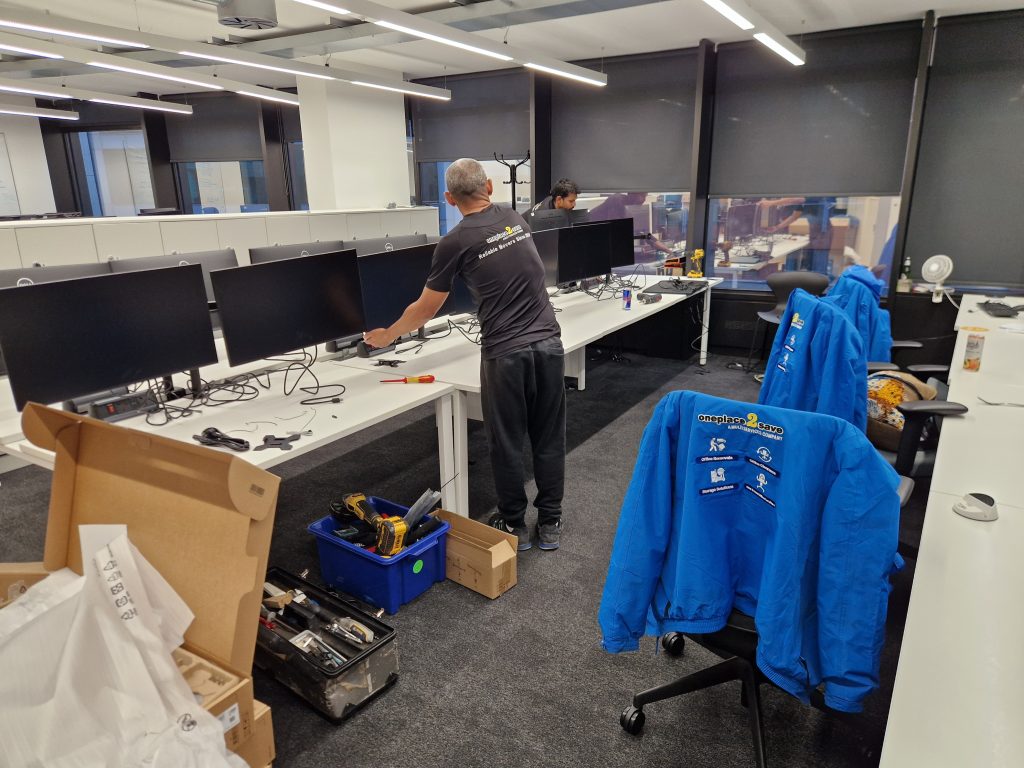 Oneplace2save team dismantling office workstations and IT equipment, disconnecting monitors and cabling during an office move.