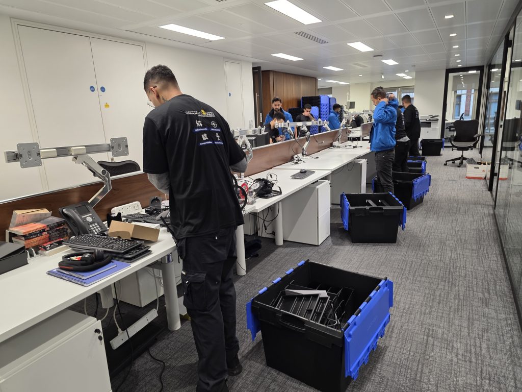 Team disconnecting monitors and desk equipment, sorting IT items into crates during an office clearance