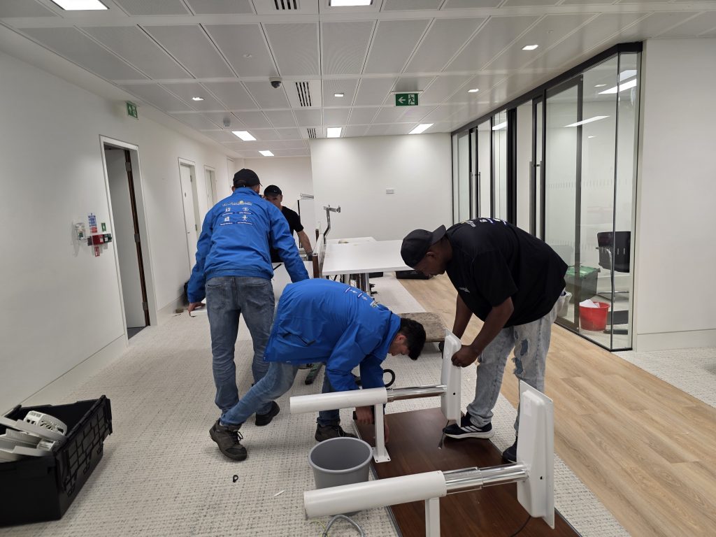 Office relocation in progress: the Oneplace2save crew carefully loads desks and office items into the removal van, using moving blankets and the tail lift to keep everything protected and secure for transport.