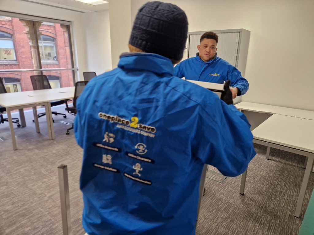 Oneplace2save team moving an office desk inside a modern workspace, relocating furniture during an office move.