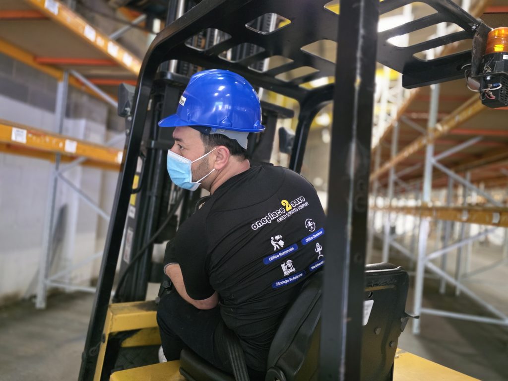 Oneplace2save team member operating a forklift inside a warehouse aisle