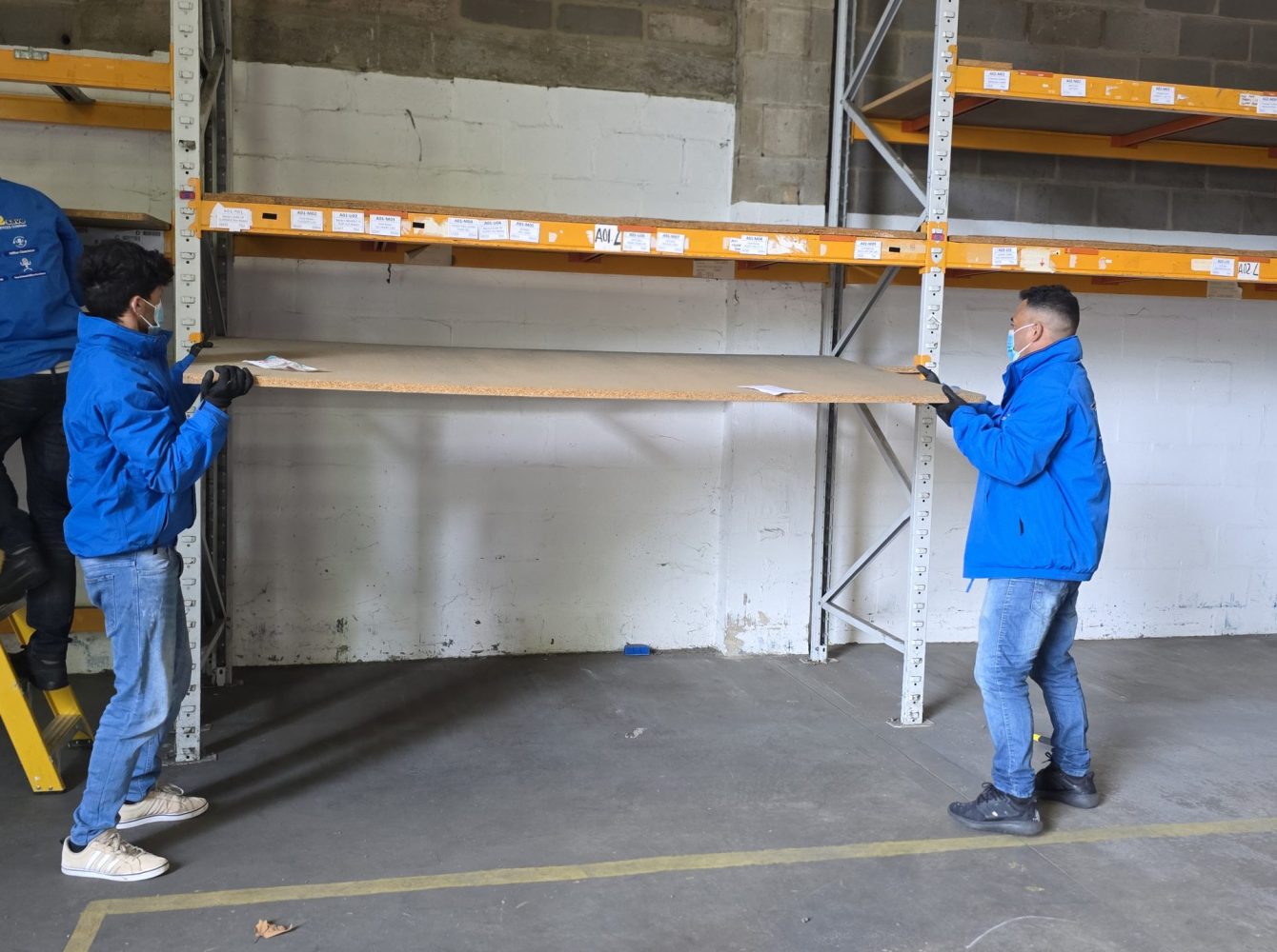 Team fitting a long shelf deck onto warehouse racking during shelving installation.